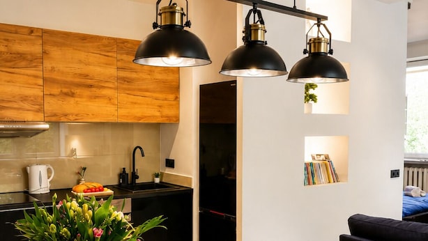 A modern kitchen with wooden cabinets, a dining table set with plates and glasses, and pendant lighting. - Lumina Apart near Museum Fryderyk Chopin (Warsaw)