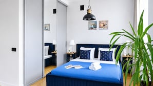 A modern bedroom with a large bed, bedside tables, a mirror, and a potted plant. - Lumina Apart near Museum Fryderyk Chopin (Warsaw)