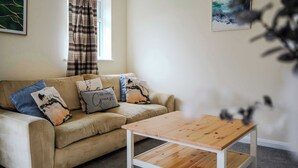 Un salon avec un canapé beige, une table basse en bois et une fenêtre avec des rideaux.
