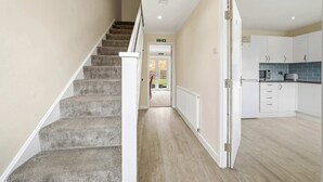 Un escalier menant à une porte, une cuisine avec des meubles blancs et un plan de travail bleu, et un couloir avec un parquet en bois clair.