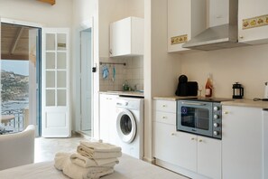 A modern kitchen with a washing machine, oven, and a view of the sea. - Melina's sunset – Cozy flat with 2 rooms, 2 baths, and bay views in Myrties (Kalymnos)