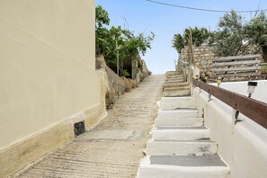 A narrow, stone-paved staircase leading up a hill, flanked by a beige wall and a white wall with a wooden railing. - Melina's sunset – Cozy flat with 2 rooms, 2 baths, and bay views in Myrties (Kalymnos)