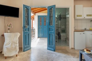Une pièce avec une télévision, une table recouverte d’une nappe, une porte bleue, un coin cuisine et une salle de bain.