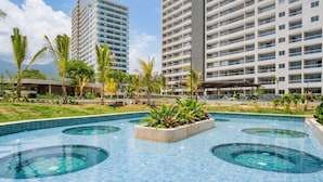 A swimming pool with multiple circular hot tubs, surrounded by palm trees and a large hotel building. - Luxury Apartment Suite With Ocean Views and Swimming Pools! (Santa Marta)