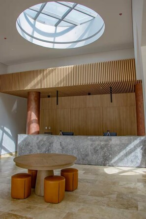 Een moderne lobby met een ronde tafel, een plafond van houten latten en een groot dakraam.
