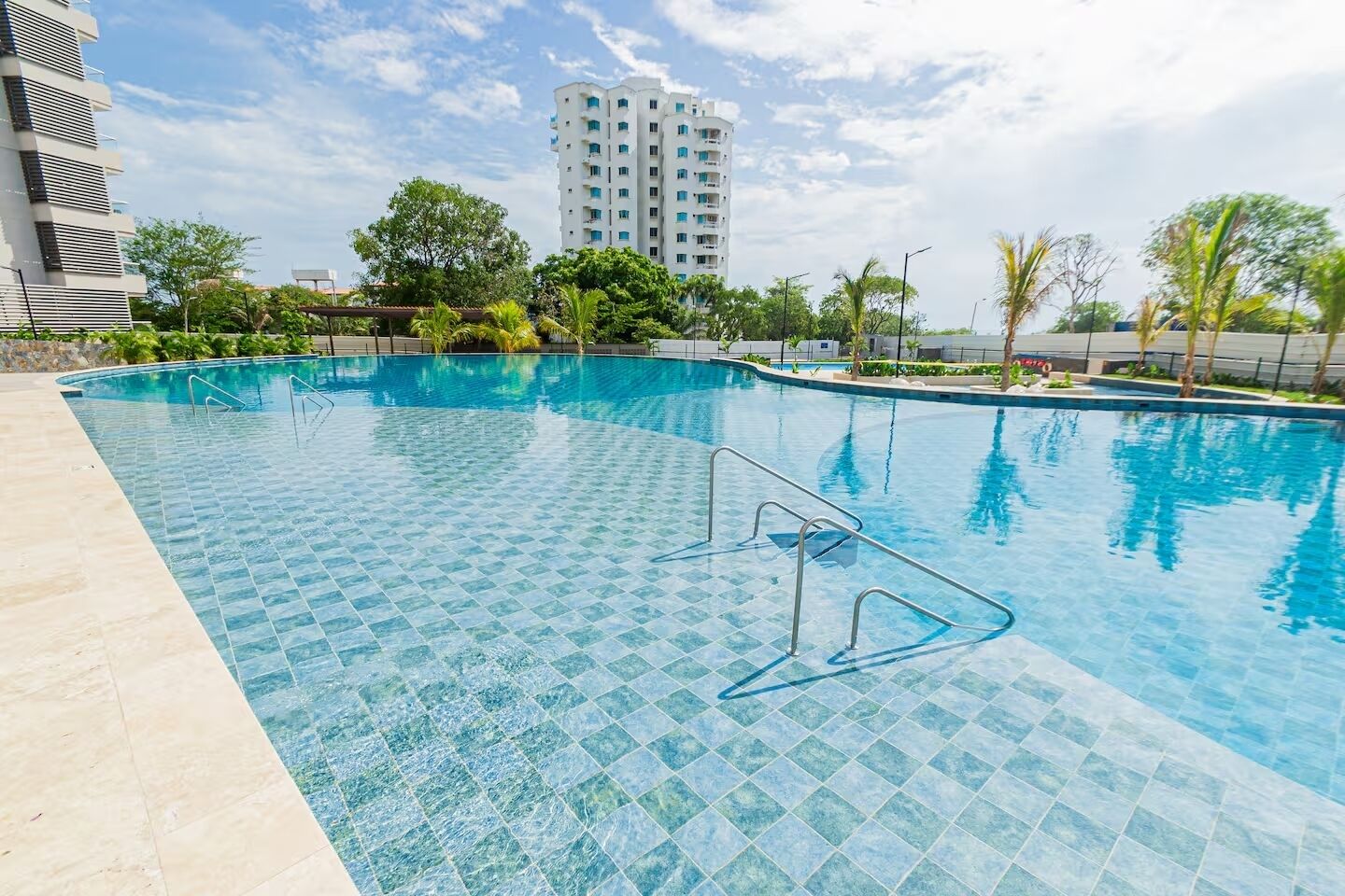 A swimming pool with clear blue water, surrounded by a tiled deck, and a tall building in the background.