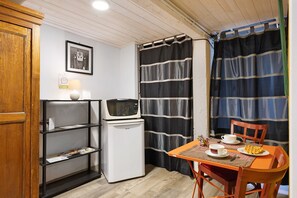 A small kitchenette with a microwave, refrigerator, and shelves. There is a table with a waffle and a cup.