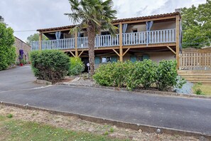 A two-story wooden building with balconies, a palm tree, and a garden.