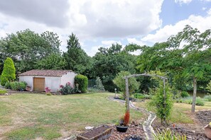 Un jardín con un cobertizo pequeño, una pérgola y diversas plantas.