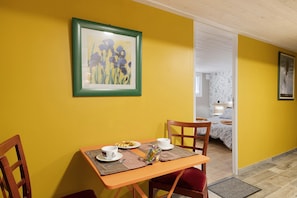 Un comedor con una mesa dispuesta para dos personas, un cuadro en la pared y una cama al fondo.