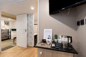 A hotel room with a wooden floor, a white door, a kitchen area with a coffee maker, a remote control, and a small cactus.