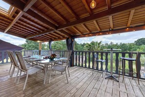 A wooden deck with a table and chairs, a railing, and a view of greenery.