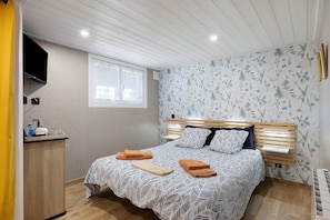 A bedroom with a bed, bedside table, window, and wall-mounted TV.