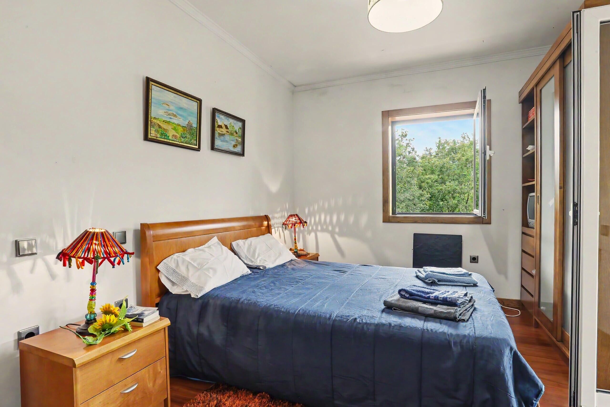 A bedroom with a bed, a nightstand, a lamp, a window, and a wardrobe.
