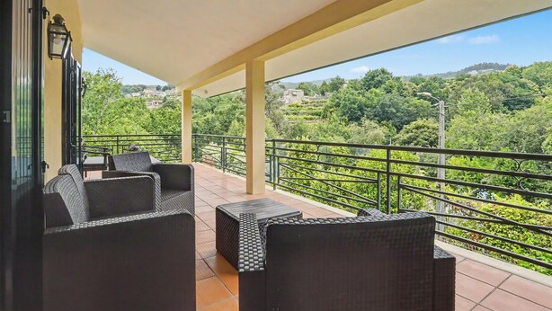 Un balcón con mobiliario de mimbre y vistas a un paisaje verde.