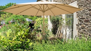 A garden with a beige umbrella, stone wall, and lush greenery. - Marine Apartment 2nd Floor Near the Beach (Cancale)
