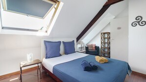 A bedroom with a skylight, a bed with blue bedding, a small table, and a chair. - Marine Apartment 2nd Floor Near the Beach (Cancale)