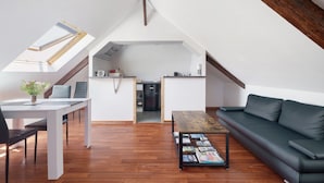 A loft-style apartment with a dining area, a sofa, a coffee table with magazines, and a kitchen in the background. - Marine Apartment 2nd Floor Near the Beach (Cancale)