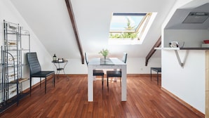 A dining area with a table and chairs, a skylight, a wooden floor, and a metal rack with items. - Marine Apartment 2nd Floor Near the Beach (Cancale)
