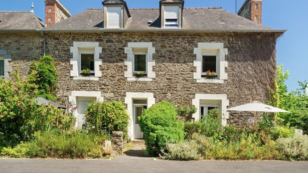 A stone building with multiple windows, a door, and a small garden area with plants and flowers. - Marine Apartment 2nd Floor Near the Beach (Cancale)