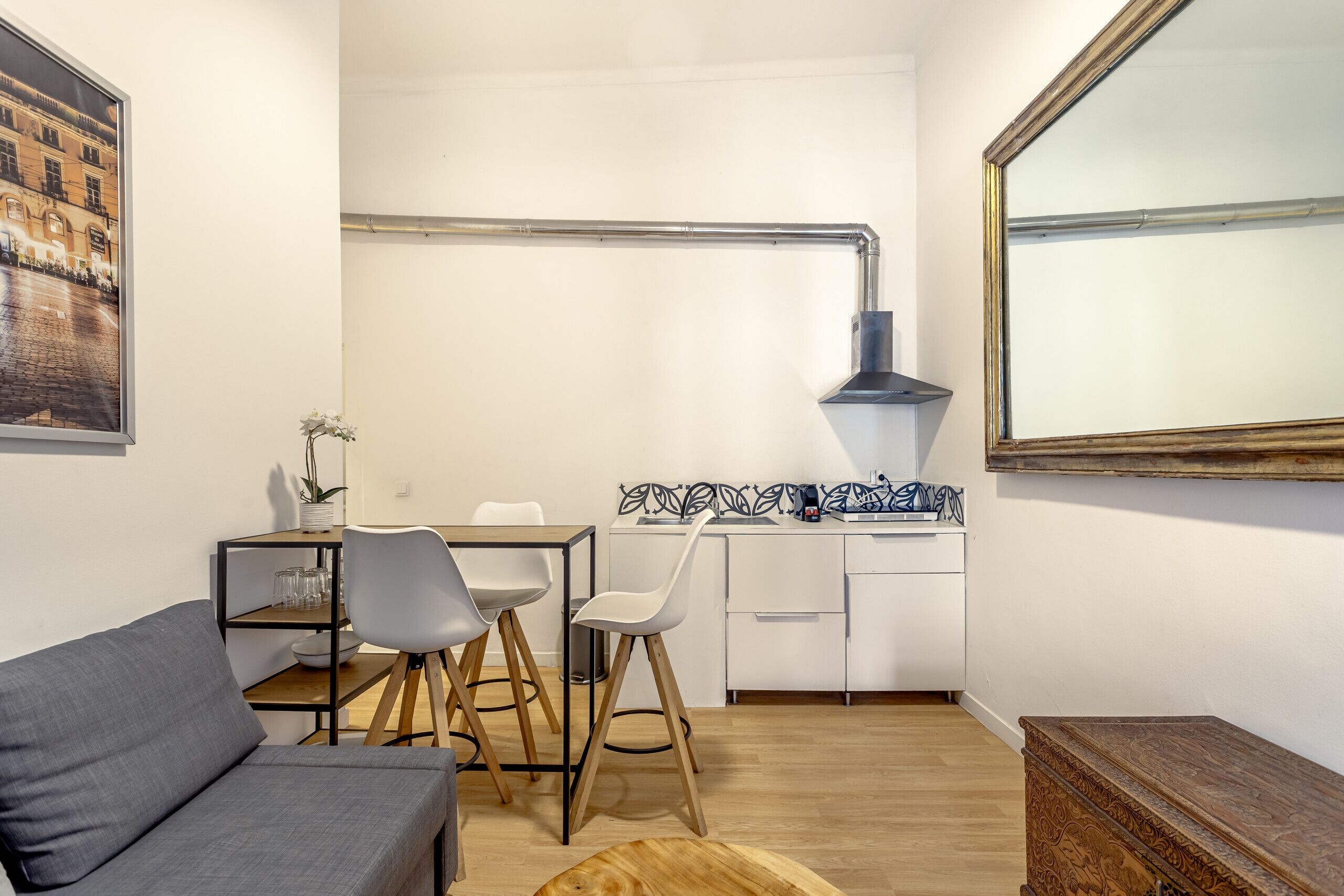 Een ruimtelijk ingerichte leefruimte met een bank, eettafel, stoelen, een klein keukentje en een grote spiegel.