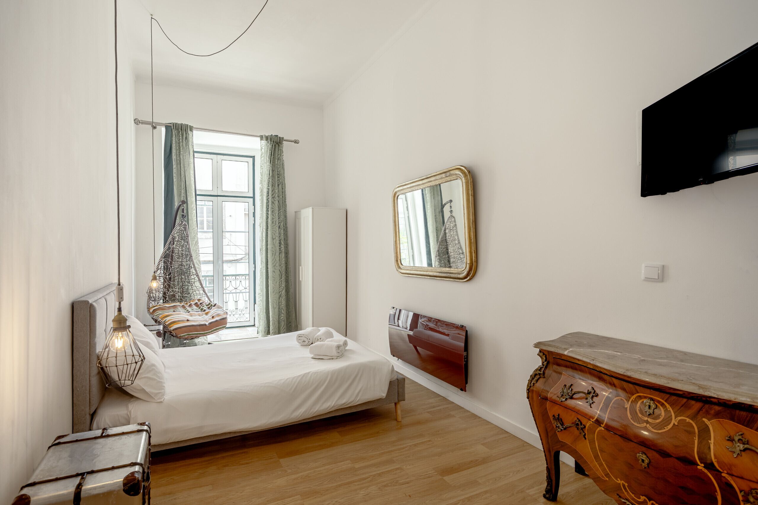 A bedroom with a bed, a dresser, a mirror, and a TV on the wall.