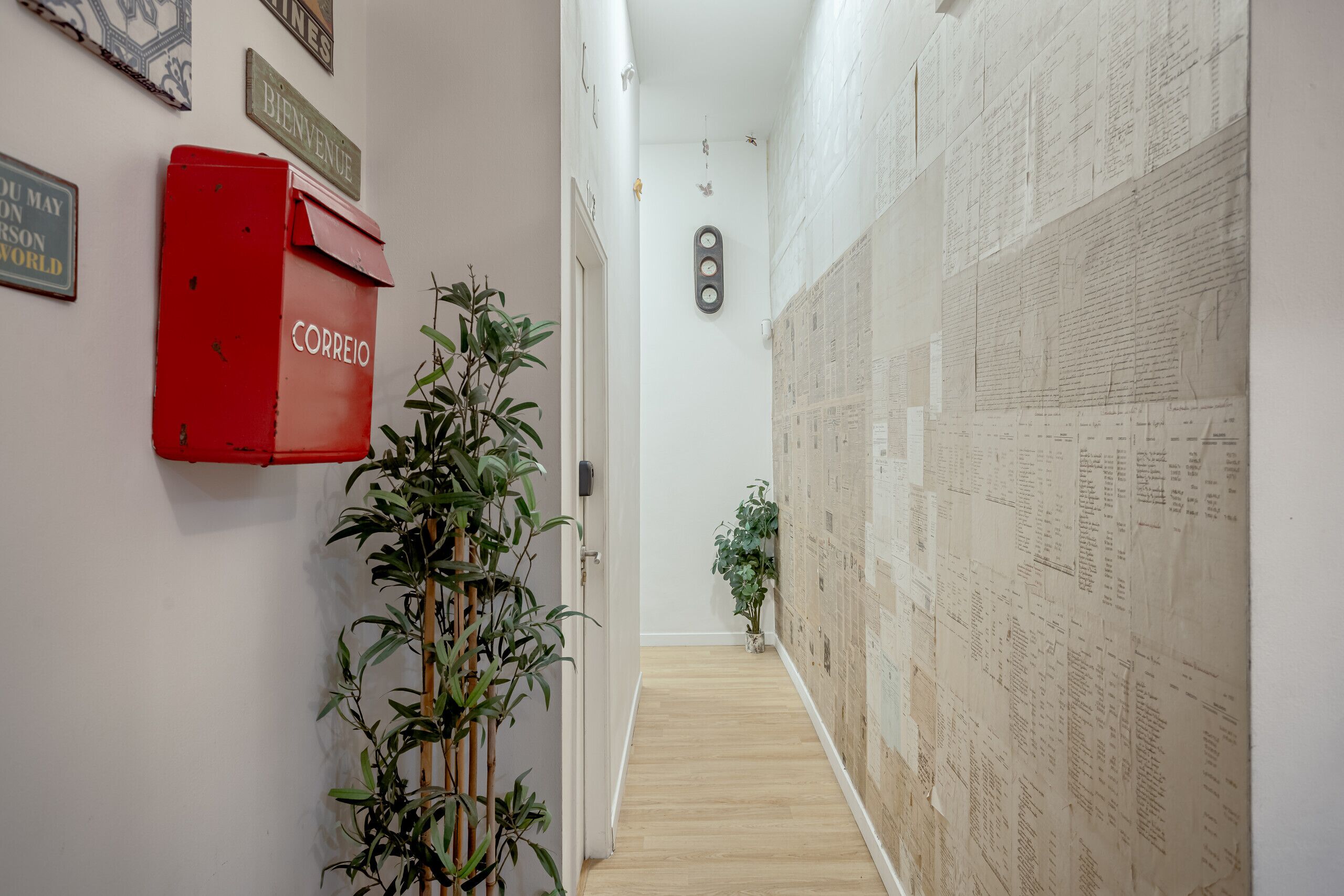 Een hal met een rode brievenbus met de tekst 'CORREIO', een plant en een muur bekleed met papieren.