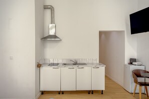 Eine kleine Küche mit weißen Schränken, einer Edelstahl-Dunstabzugshaube, einem Spülbecken und einem kleinen Kühlschrank.