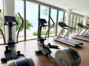 Een fitnessruimte met cardioapparatuur, grote ramen en uitzicht op het strand.