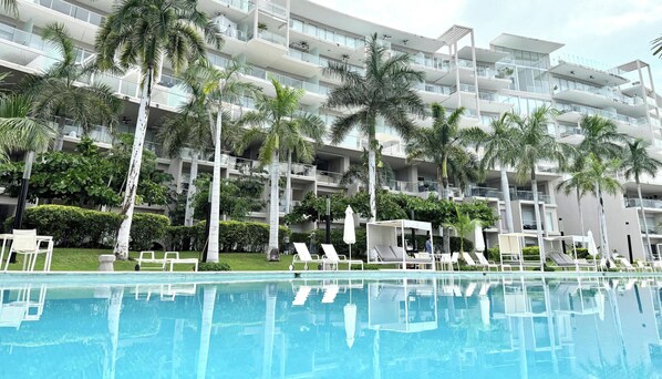 Een meerlaags hotel met balkons, een zwembad en palmbomen.