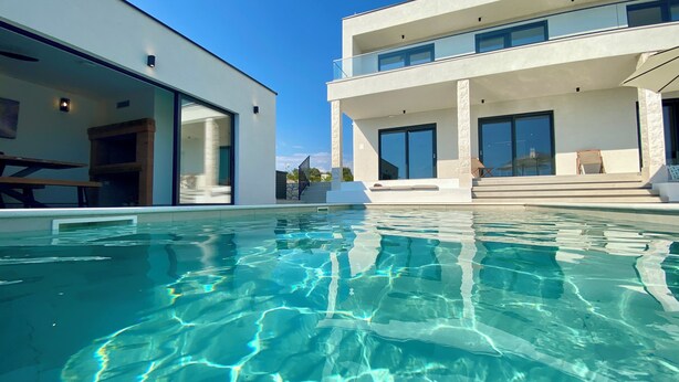 Et moderne hus med swimmingpool, store vinduer og en balkon.