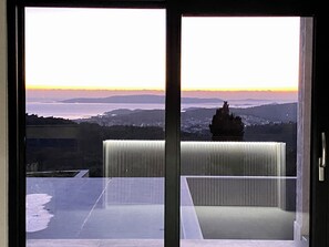 Ein Zimmer mit Blick auf einen Sonnenuntergang über einem Gewässer und sanfte Hügel in der Ferne.