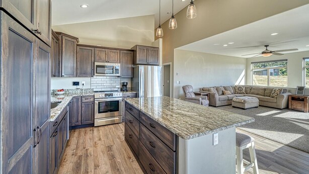 A spacious kitchen with dark wood cabinets, a granite countertop, stainless steel appliances, and pendant lighting. - Spacious mountain chalet with breathtaking views on all sides, just 15 minutes from Monarch Ski Area and 15 minutes from downtown Salida. (Salida)