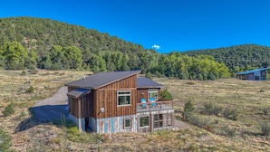 A wooden cabin with a balcony, surrounded by a grassy field and forested hills. - Spacious mountain chalet with breathtaking views on all sides, just 15 minutes from Monarch Ski Area and 15 minutes from downtown Salida. (Salida)