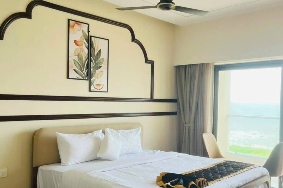 Habitación de hotel con una cama, un ventilador de techo, un ventanal con vistas y una obra de arte enmarcada en la pared.