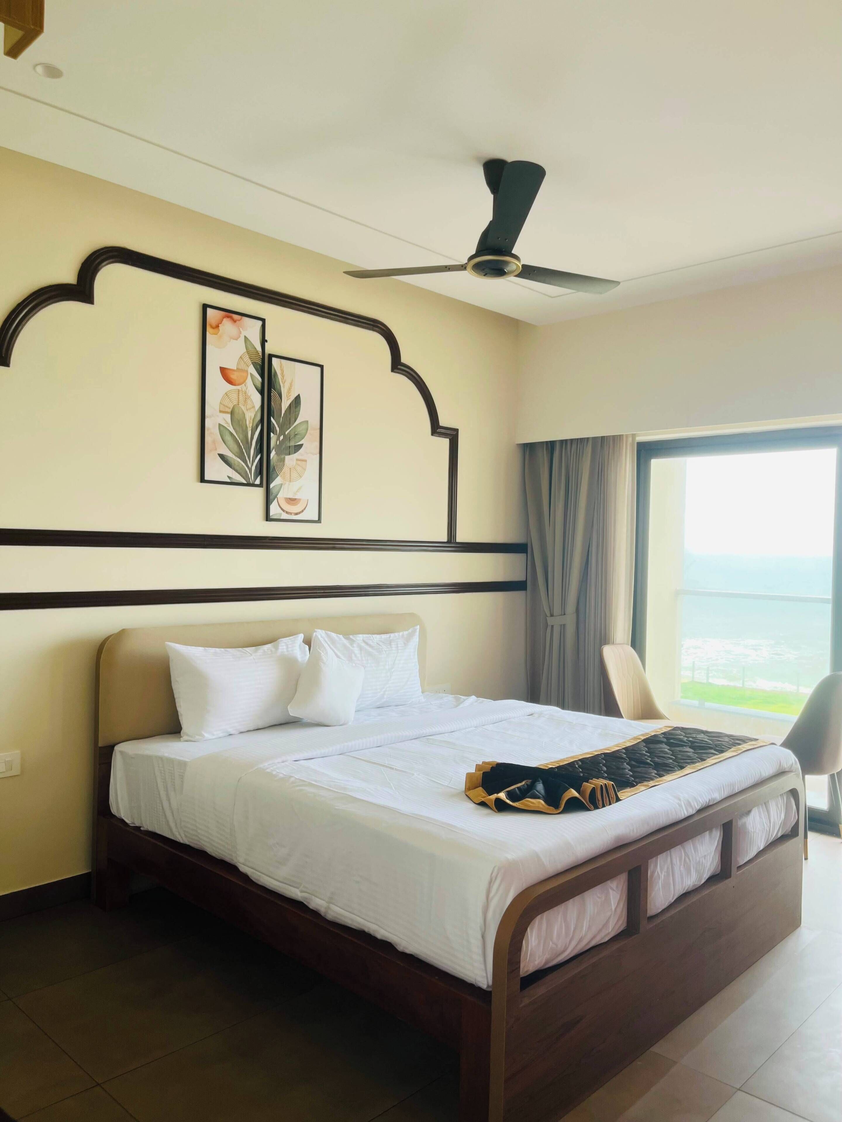 A hotel room with a bed, a ceiling fan, a window with curtains, and a wall-mounted artwork.