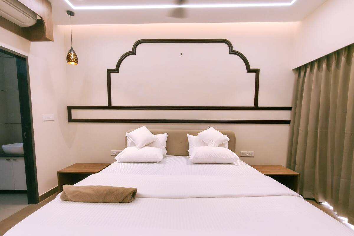 Una cama bien hecha con ropa blanca y almohadas, un cabecero de madera, mesitas de noche y una lámpara colgante.