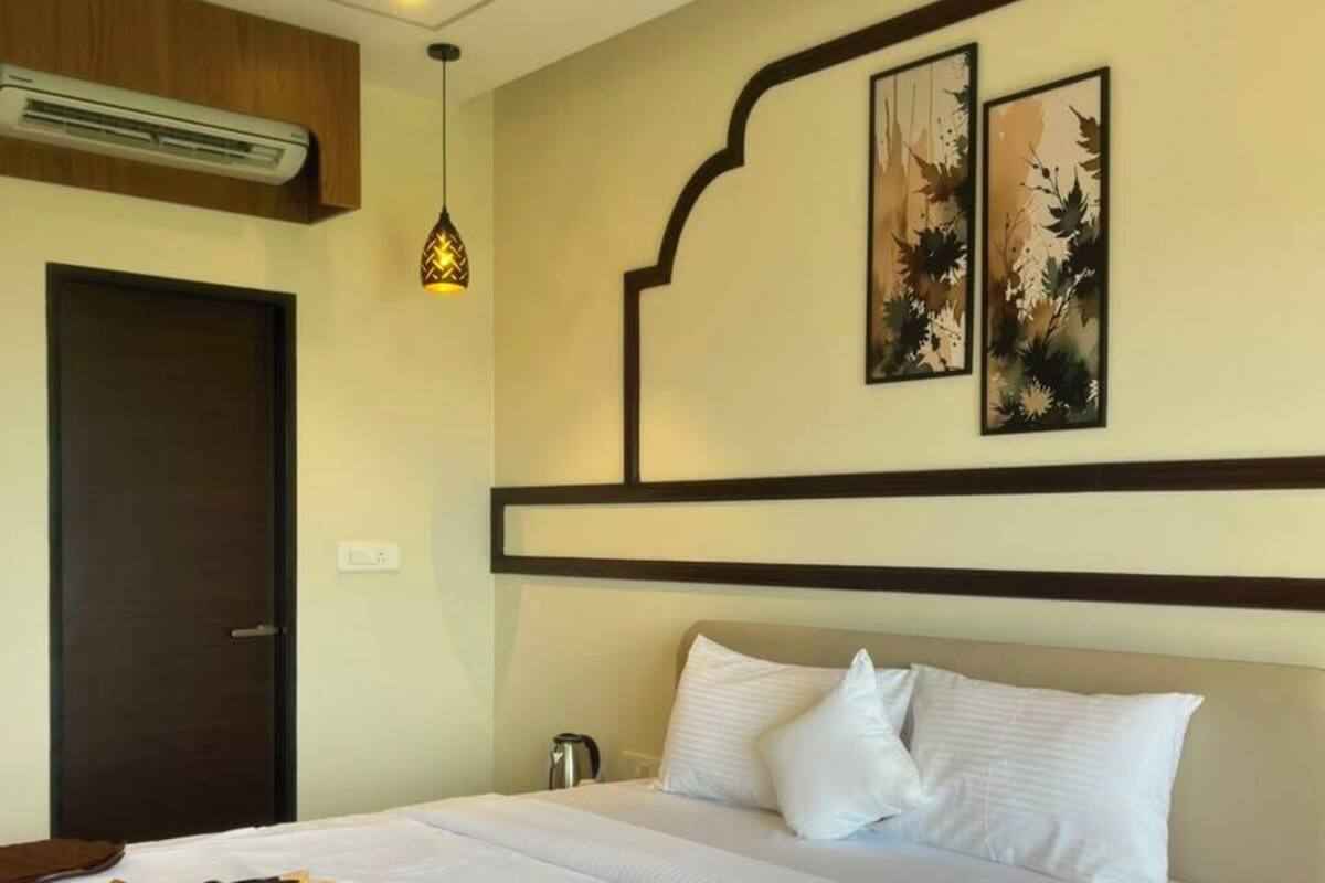 Habitación de hotel con cama, ventilador de techo, aire acondicionado y dos cuadros enmarcados.