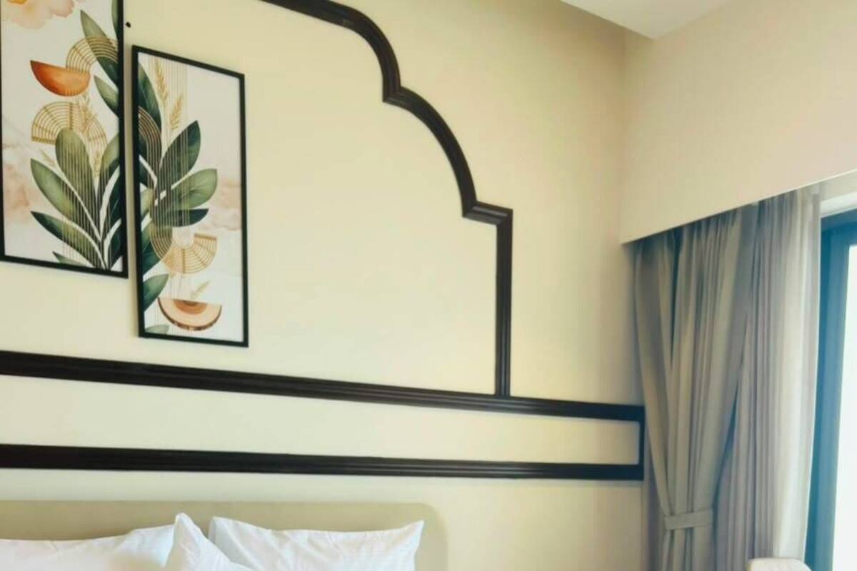 Una habitación de hotel con una cama grande, cabecera, una silla y una ventana con cortinas.