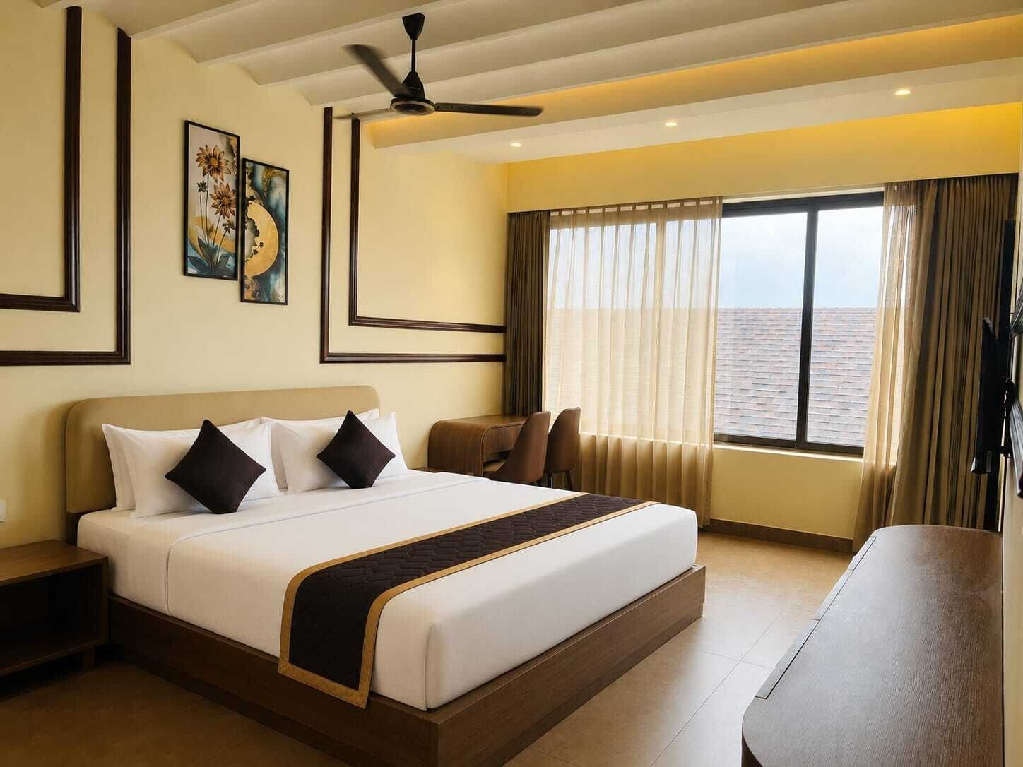 A hotel room with a large bed, a desk, a ceiling fan, and a window with curtains.