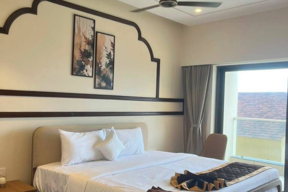 Habitación de hotel con cama, ventilador de techo, mesita de noche, una silla y ventana con vistas.