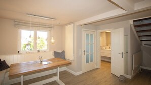 Um quarto com uma mesa de madeira, um banco, uma janela com cortinas, uma porta e uma escada.