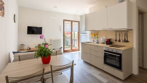 Eine moderne Küche mit Einbauofen, eine Essecke mit Tisch und Stühlen sowie ein großes Fenster mit Jalousien.