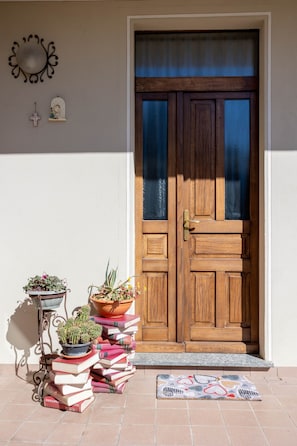 A wooden door with a glass panel, a metal wall decoration, and a small shelf with a cross and a figurine. - Apartment 'La Casa Del Borgo' with Balcony and Wi-Fi (Orta San Giulio)