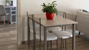 Ein Essbereich mit einem Holztisch, vier Stühlen, einem roten Blumentopf und drei Wandbildern zum Thema Kaffee.