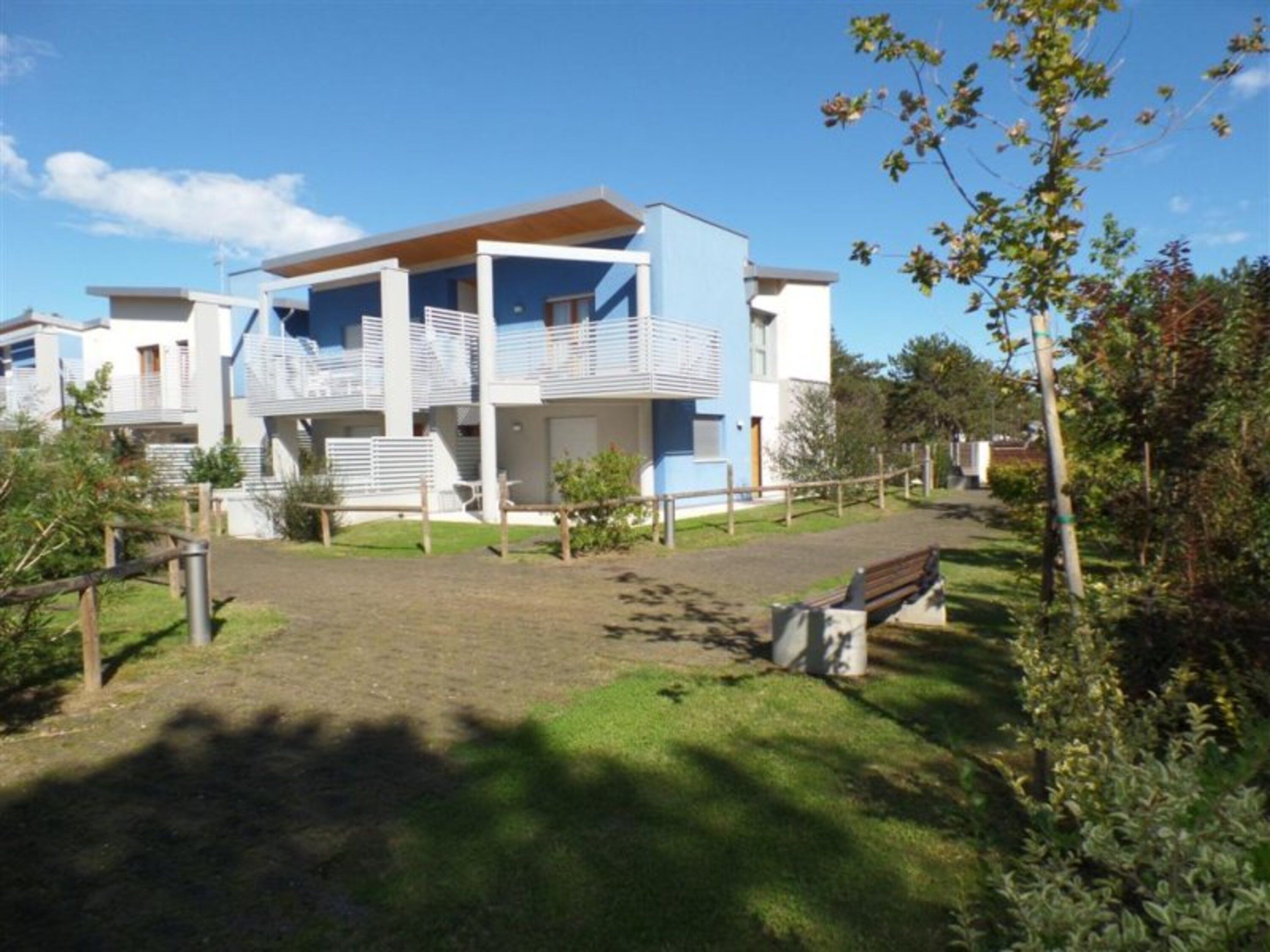 A modern multi-story building with balconies, a grassy courtyard, and a wooden fence.