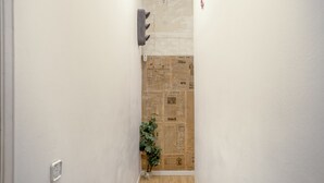 Un pasillo estrecho con suelo de madera, un aplique y una planta.