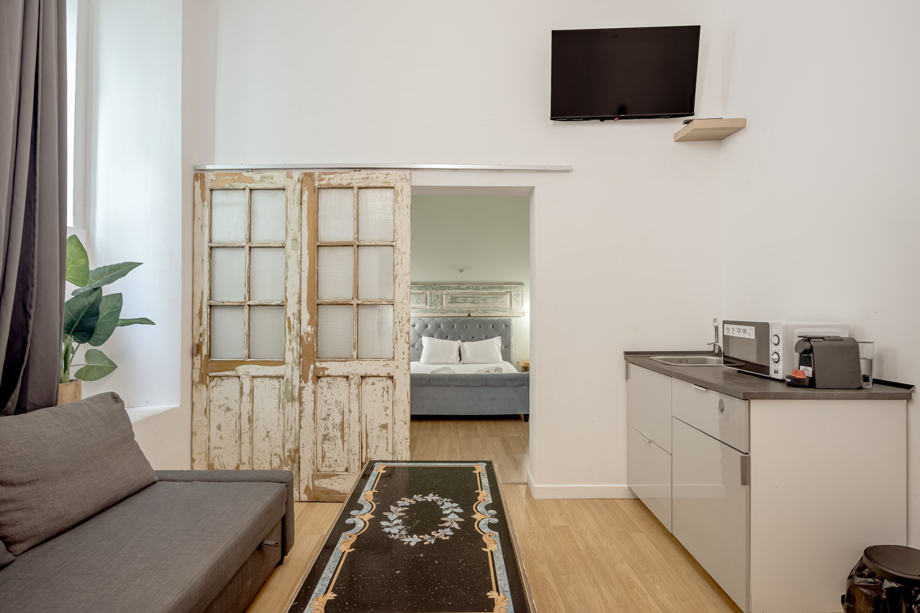 A compact living space with a sofa, a kitchen area with a microwave, a television, and a large window with curtains.