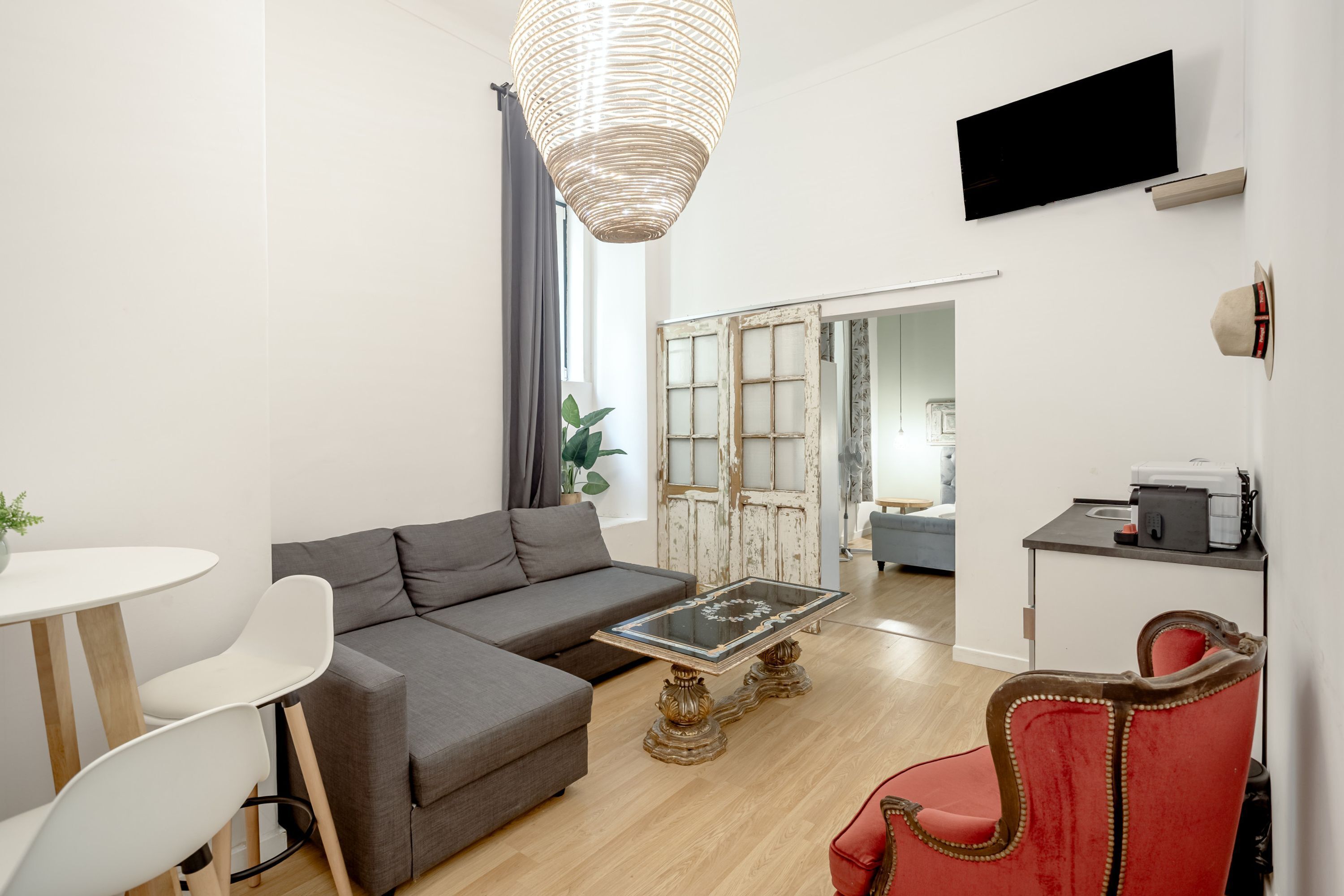 A modern living room with a sofa, a glass coffee table, a red chair, a television, and a sliding door leading to another room.