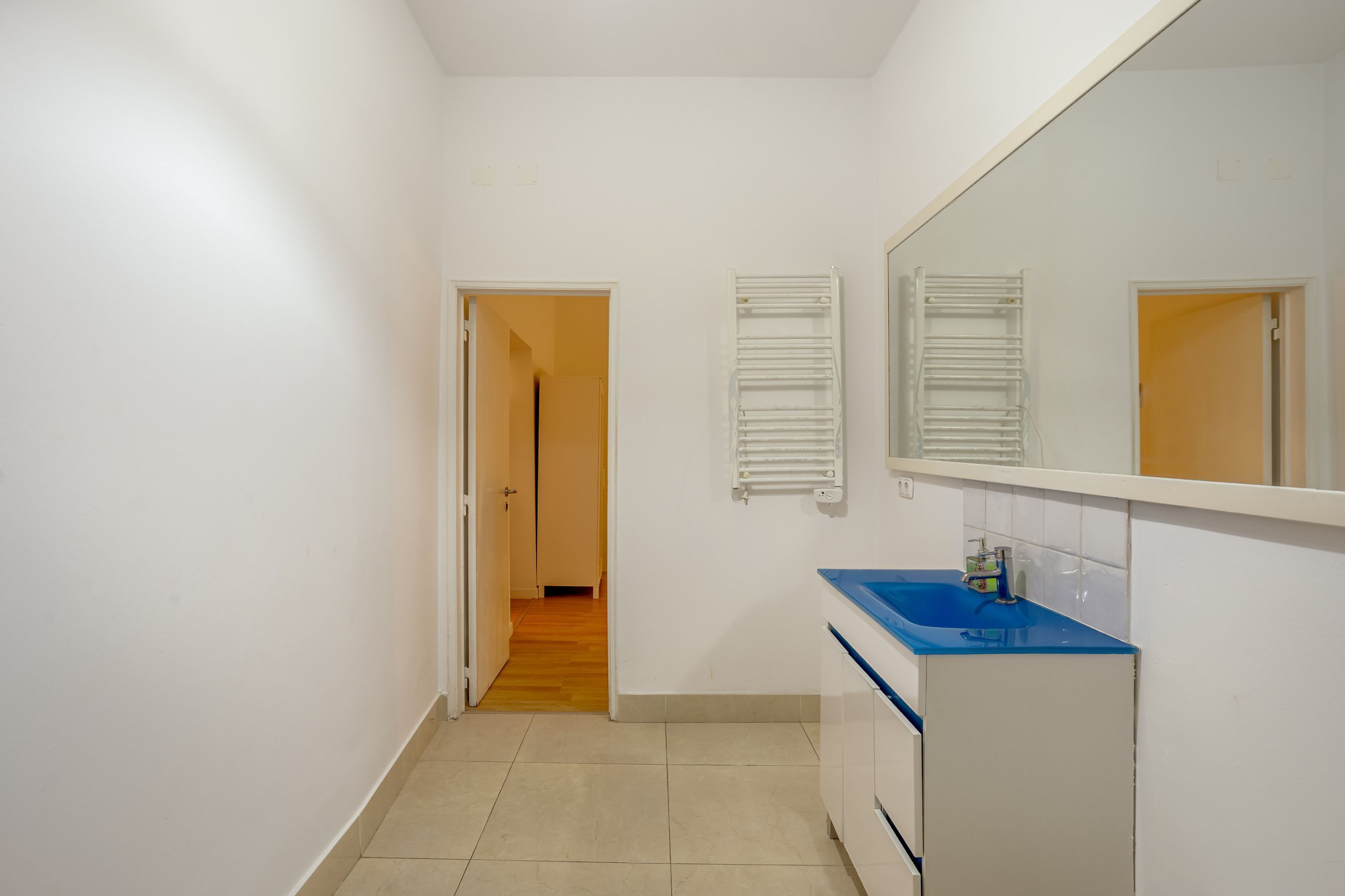A narrow hallway leading to a bathroom with a sink, mirror, and towel racks.